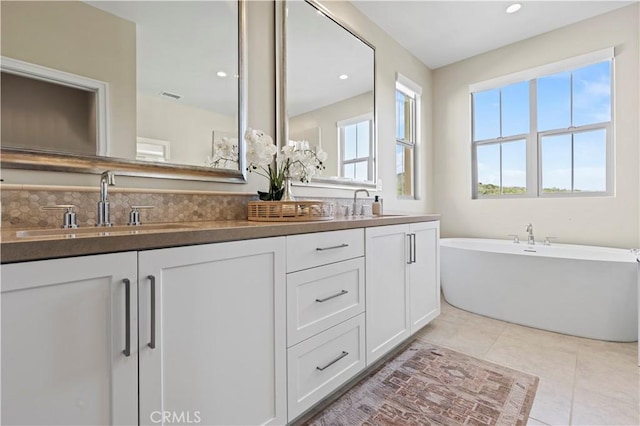 bathroom featuring a sink, tile patterned flooring, double vanity, visible vents, and a soaking tub