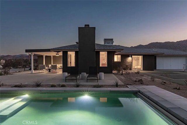 back of house at dusk featuring a mountain view, a chimney, an outdoor pool, and a patio area