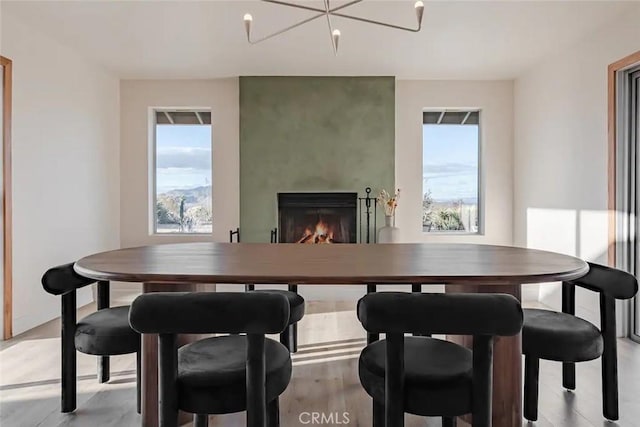 dining space with light wood-style floors, a healthy amount of sunlight, a lit fireplace, and an inviting chandelier