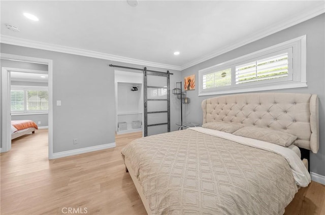 bedroom with light wood-type flooring, a barn door, crown molding, and multiple windows