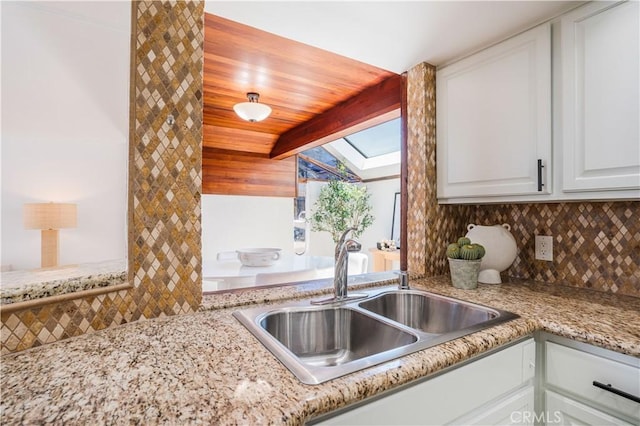 kitchen with white cabinets, light stone countertops, a sink, tasteful backsplash, and lofted ceiling with skylight