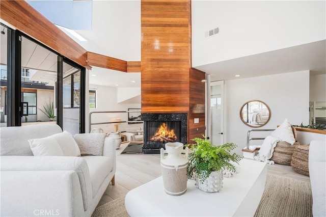 living area featuring visible vents, a high ceiling, a multi sided fireplace, and wood finished floors