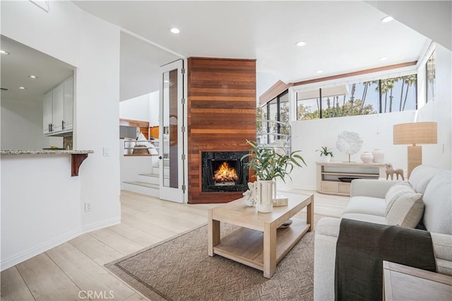living area featuring stairs, recessed lighting, a warm lit fireplace, and light wood-style floors