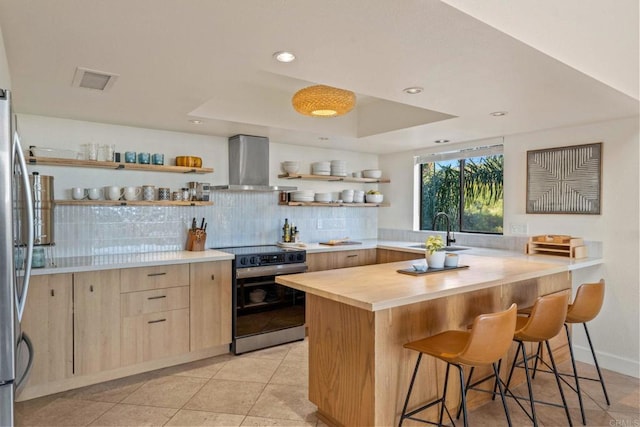 kitchen with open shelves, light brown cabinets, a kitchen breakfast bar, wall chimney range hood, and electric stove
