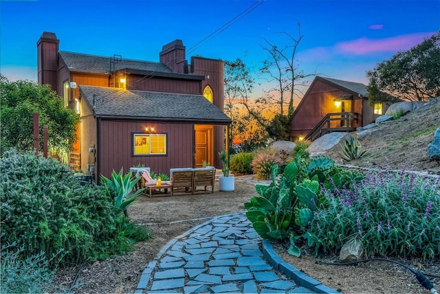 back of house at dusk with a shingled roof, an outdoor hangout area, a patio, and a chimney