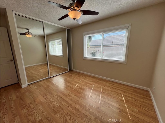 unfurnished bedroom featuring baseboards, a closet, light wood-type flooring, and a textured ceiling