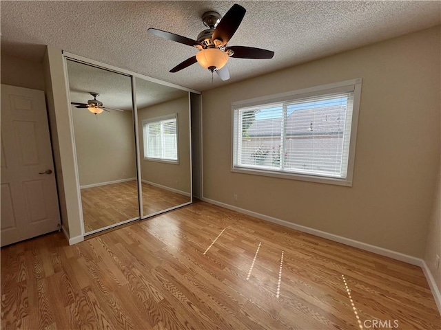 unfurnished bedroom featuring a closet, baseboards, light wood-type flooring, a textured ceiling, and a ceiling fan
