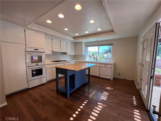 kitchen with wooden counters, white cabinets, a tray ceiling, recessed lighting, and white appliances