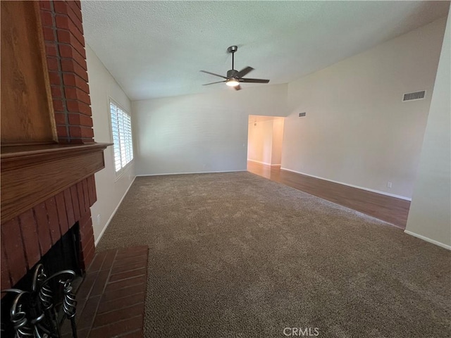 unfurnished living room featuring ceiling fan, visible vents, a fireplace, vaulted ceiling, and carpet floors