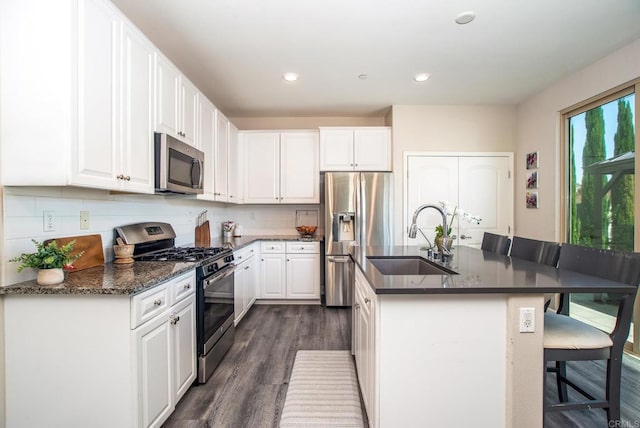 kitchen with a sink, appliances with stainless steel finishes, dark wood-style floors, and white cabinetry