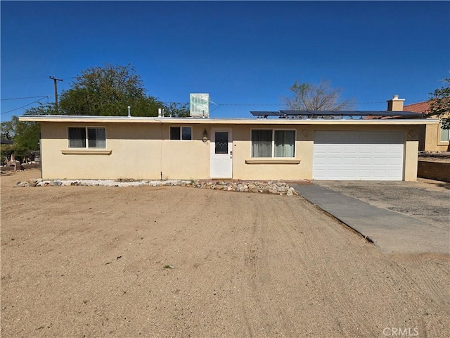 single story home featuring an attached garage, driveway, solar panels, and stucco siding