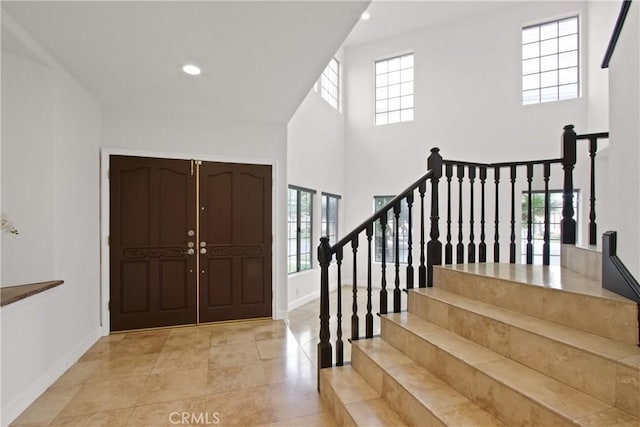 entrance foyer with light tile patterned flooring, baseboards, stairway, and a towering ceiling