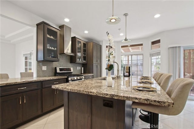 kitchen featuring a kitchen bar, stainless steel range with gas stovetop, a sink, light tile patterned floors, and wall chimney exhaust hood