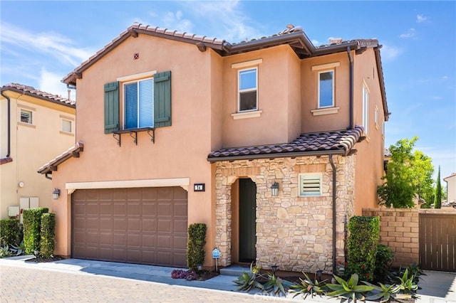 mediterranean / spanish house with an attached garage, stucco siding, a tile roof, and stone siding