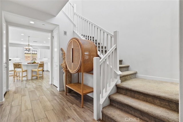 stairway with visible vents, an inviting chandelier, wood finished floors, baseboards, and recessed lighting