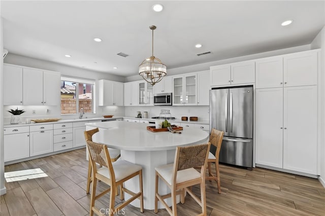 kitchen with visible vents, glass insert cabinets, a kitchen bar, light countertops, and appliances with stainless steel finishes