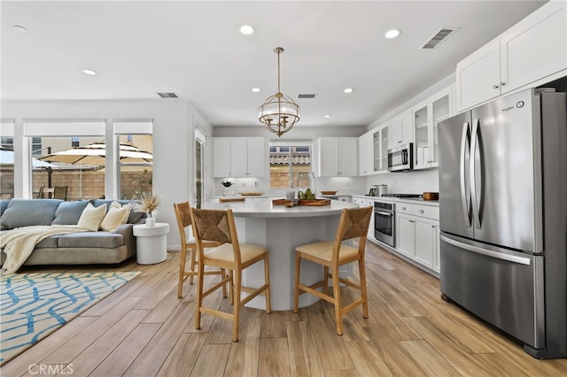 kitchen with appliances with stainless steel finishes, light countertops, open floor plan, visible vents, and glass insert cabinets