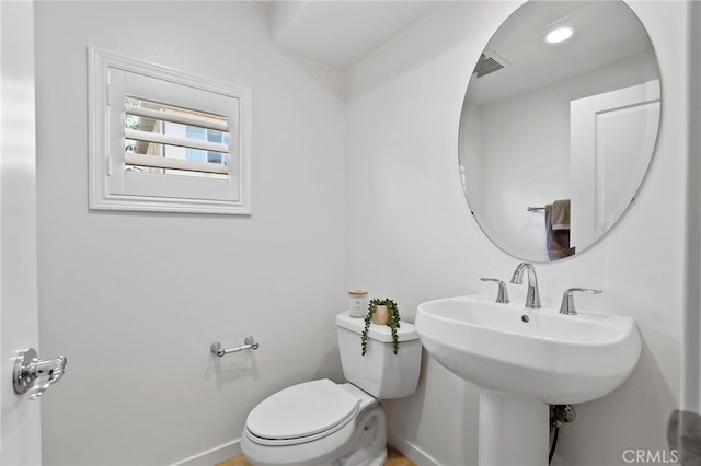half bath featuring toilet, baseboards, visible vents, and a sink
