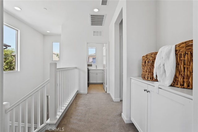 corridor with an upstairs landing, plenty of natural light, and visible vents