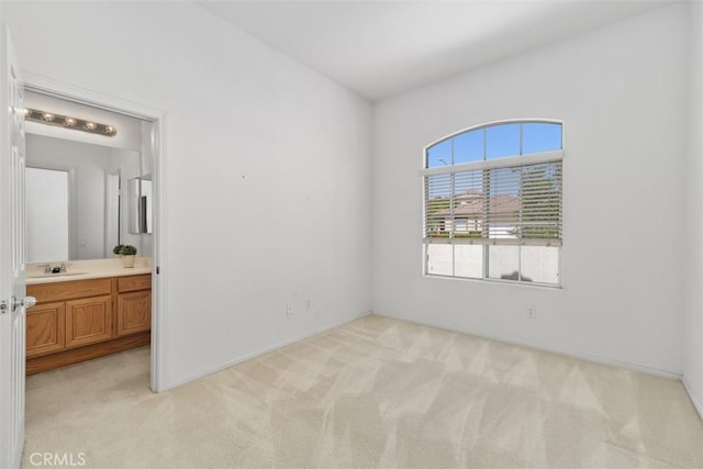 unfurnished bedroom featuring ensuite bathroom, a sink, and light carpet
