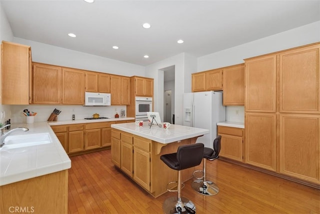 kitchen featuring a sink, light wood-style floors, white appliances, a breakfast bar area, and a kitchen island