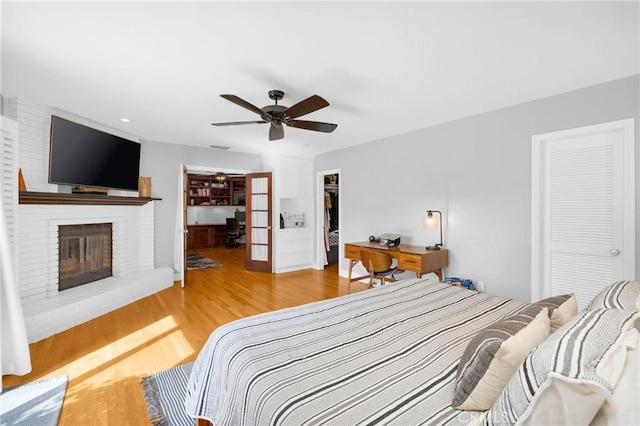 bedroom with a closet, wood finished floors, a fireplace, a spacious closet, and a ceiling fan