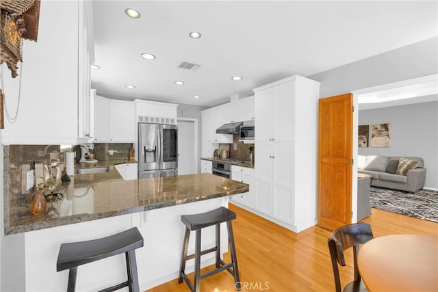 kitchen featuring appliances with stainless steel finishes, a sink, light wood finished floors, under cabinet range hood, and visible vents