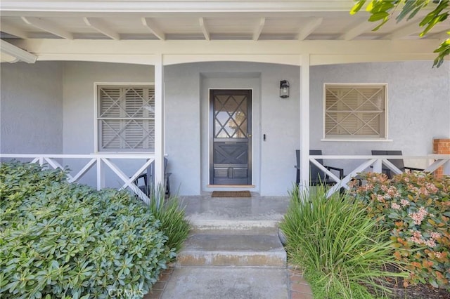 property entrance with covered porch and stucco siding
