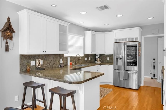 kitchen with visible vents, a peninsula, white cabinets, stainless steel fridge with ice dispenser, and a sink