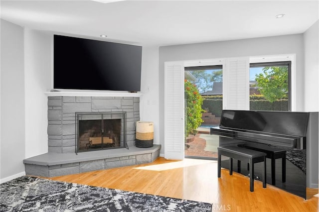 sitting room featuring baseboards, a stone fireplace, recessed lighting, and wood finished floors