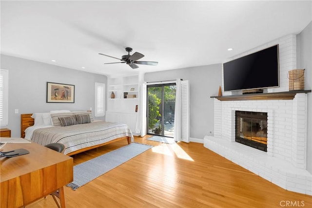 bedroom with access to outside, a brick fireplace, recessed lighting, and wood finished floors