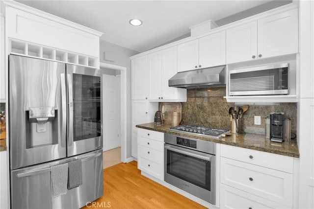 kitchen featuring under cabinet range hood, white cabinets, tasteful backsplash, light wood-style flooring, and stainless steel appliances