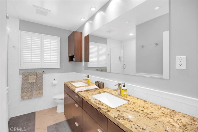 full bath featuring vanity, toilet, tile patterned floors, tile walls, and a shower with door
