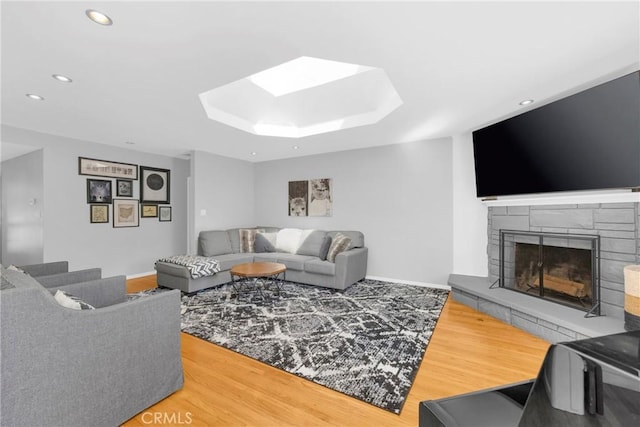 living area featuring a fireplace, recessed lighting, baseboards, wood finished floors, and a skylight