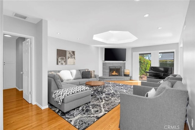 living area with a stone fireplace, visible vents, a skylight, wood finished floors, and baseboards
