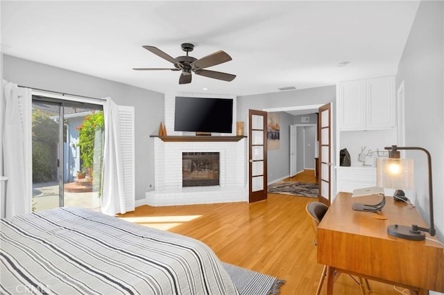 bedroom featuring a brick fireplace, access to exterior, baseboards, light wood-type flooring, and visible vents