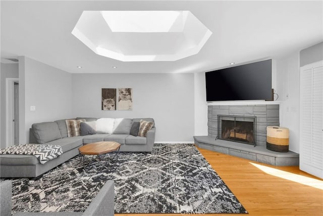 living room featuring a stone fireplace, a skylight, wood finished floors, a tray ceiling, and recessed lighting