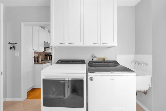 laundry room with light tile patterned floors, baseboards, washing machine and dryer, and cabinet space