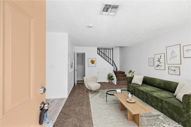 carpeted living area featuring a textured ceiling, visible vents, and stairway