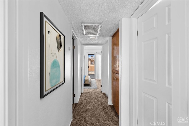 corridor with dark colored carpet, a textured ceiling, and visible vents