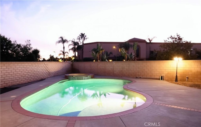 pool at dusk featuring a pool with connected hot tub, a fenced backyard, and a patio area