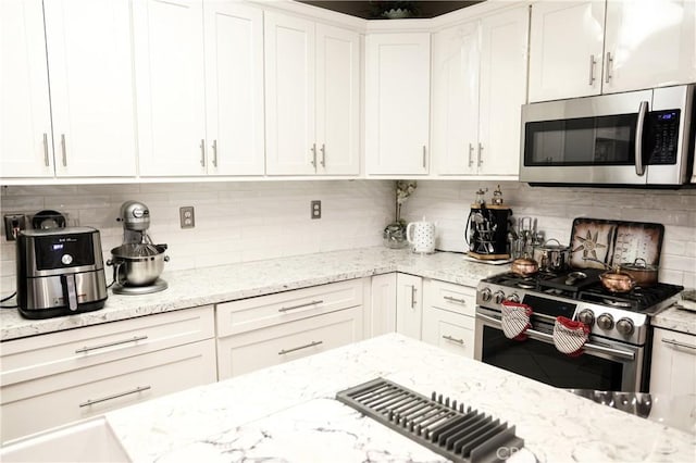 kitchen featuring light stone counters, decorative backsplash, white cabinetry, and appliances with stainless steel finishes