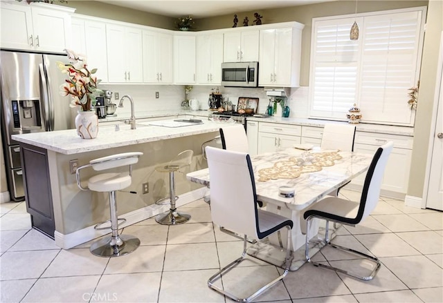 kitchen with light stone countertops, a breakfast bar, stainless steel appliances, white cabinetry, and a center island with sink