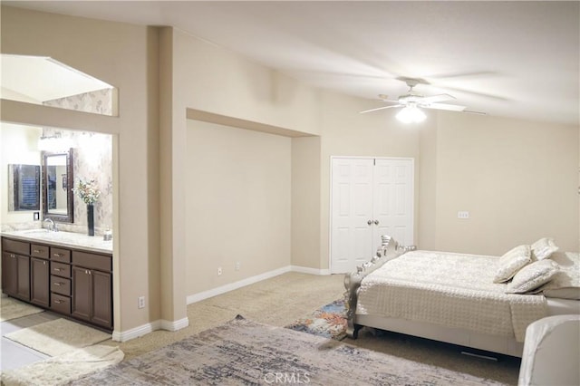 bedroom featuring a closet, baseboards, light colored carpet, a sink, and ensuite bath