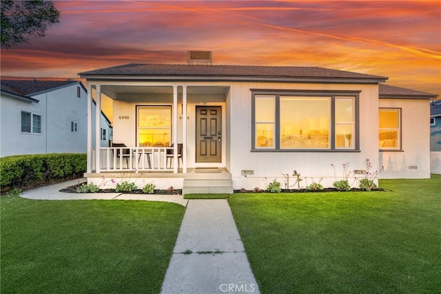 bungalow-style home with covered porch, a shingled roof, and a yard