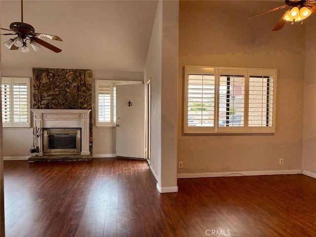 unfurnished living room with baseboards, a stone fireplace, a ceiling fan, and wood finished floors