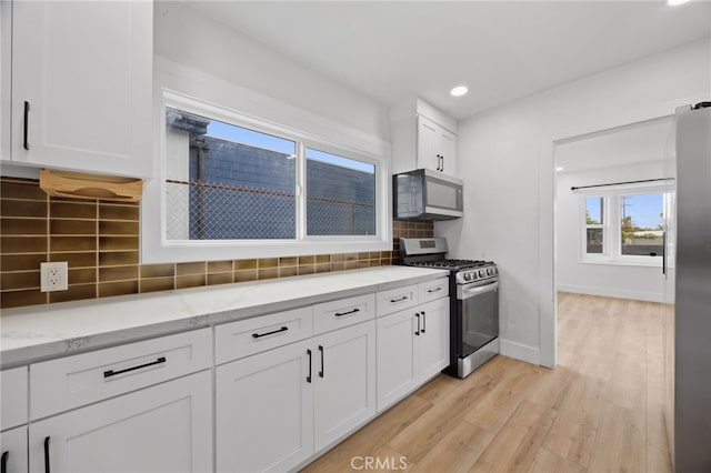 11867 S San Pedro St, Los Angeles, CA 90061 - kitchen featuring white cabinets, stainless steel appliances, light wood finished floors, and tasteful backsplash