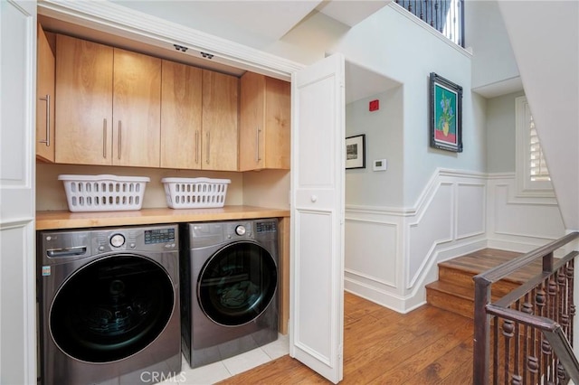 laundry room featuring washer and dryer, cabinet space, wainscoting, light wood-style floors, and a healthy amount of sunlight