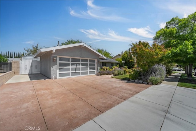 exterior space featuring fence, an attached garage, stucco siding, a gate, and driveway
