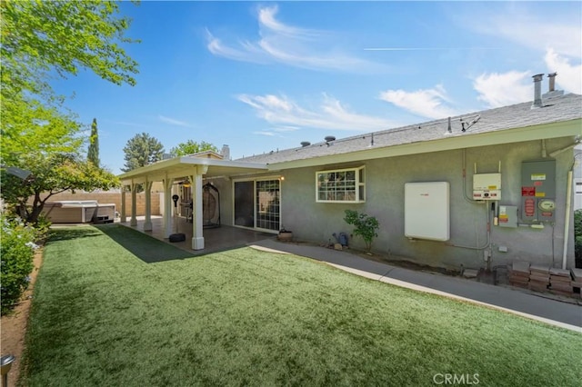 rear view of house with a patio, a hot tub, stucco siding, and a lawn